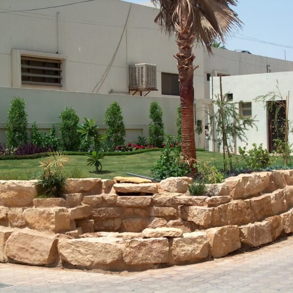 حجارة طبيعية مرتبة بشكل جمالي في تصميم حديقة مع نباتات خضراء وأشجار.