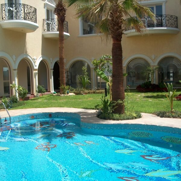 مسبح مزين برسوم ملونة للأسماك في فناء داخلي مع أشجار النخيل.