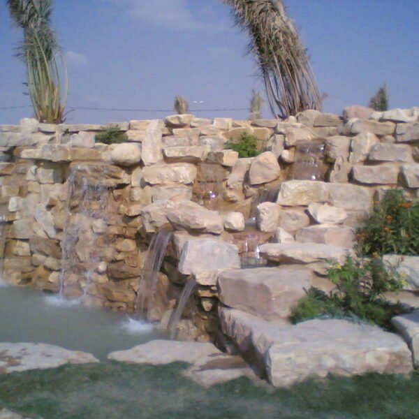 شلال مائي يتدفق من بين الصخور الطبيعية مع نباتات خضراء في محيطه.