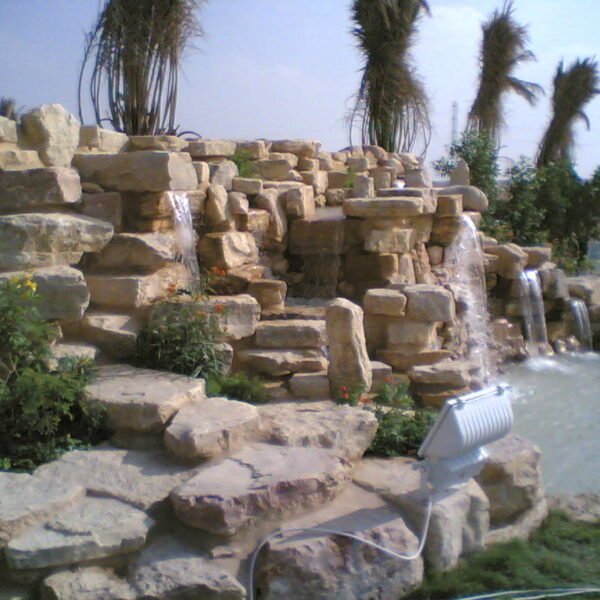 شلالات مائية تتدفق من الصخور الطبيعية مع نباتات مزهرة حولها.