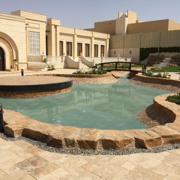 بركة مياه دائرية محاطة بحجارة طبيعية في حديقة مع نباتات مزهرة.