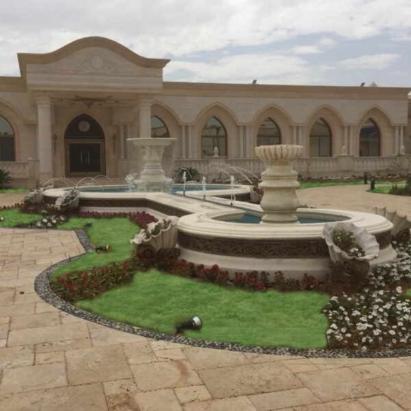 فناء مزين بنافورة حجرية وحديقة مزهرة مع مساحات خضراء في تصميم خارجي.