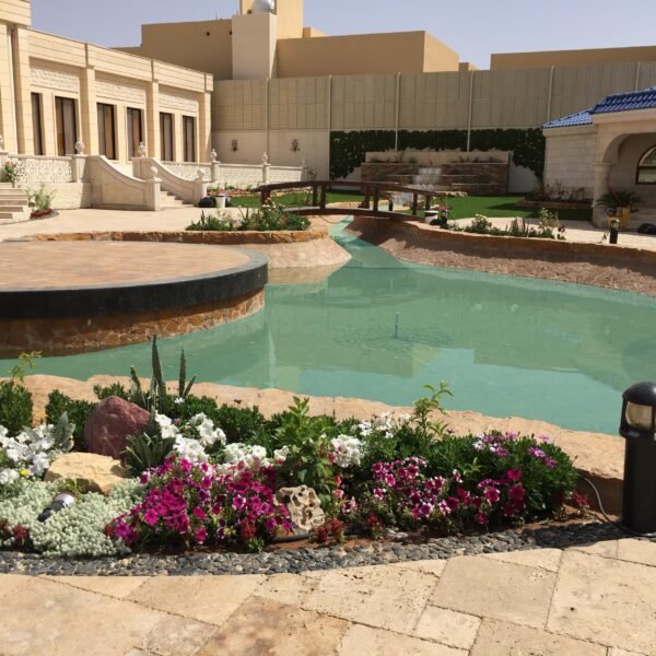 بركة مياه محاطة بأزهار ملونة ونباتات خضراء في حديقة منسقة.